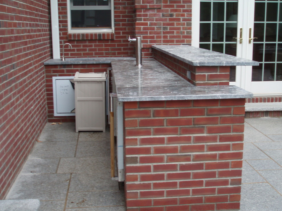Cette photo montre une grande terrasse arrière chic avec une cuisine d'été, des pavés en pierre naturelle et aucune couverture.