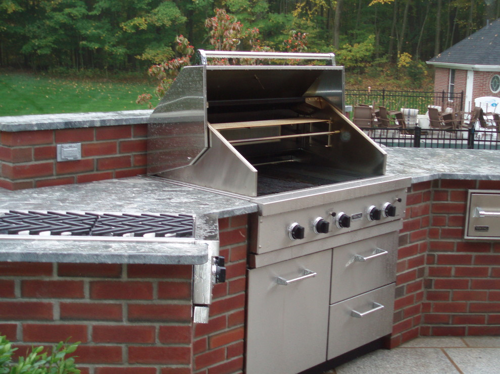 Cette image montre une grande terrasse arrière traditionnelle avec une cuisine d'été, des pavés en pierre naturelle et aucune couverture.