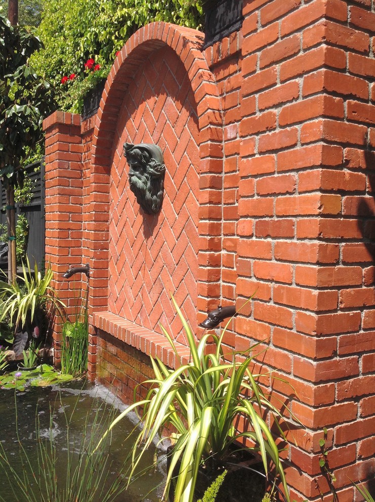 Diseño de patio clásico grande en patio trasero con fuente, adoquines de ladrillo y pérgola