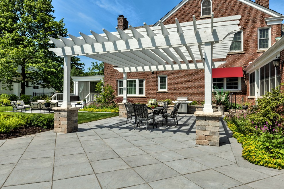 Aménagement d'une grande terrasse arrière classique avec un foyer extérieur, des pavés en pierre naturelle et une pergola.
