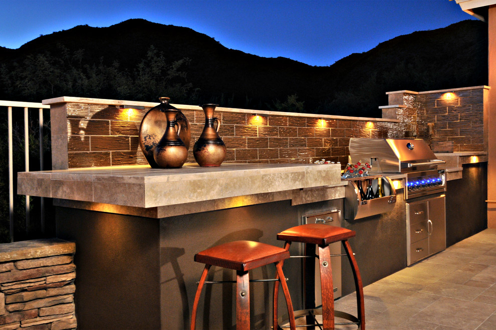 This is an example of a traditional back patio in Phoenix with an outdoor kitchen and natural stone paving.