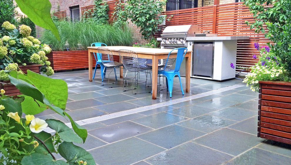 Réalisation d'une terrasse avec des plantes en pots arrière design avec des pavés en pierre naturelle.
