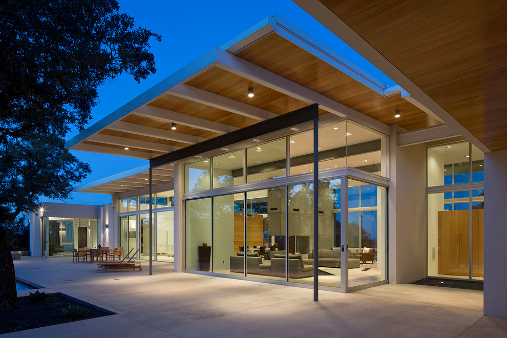 Réalisation d'une grande terrasse arrière minimaliste avec une dalle de béton et une extension de toiture.