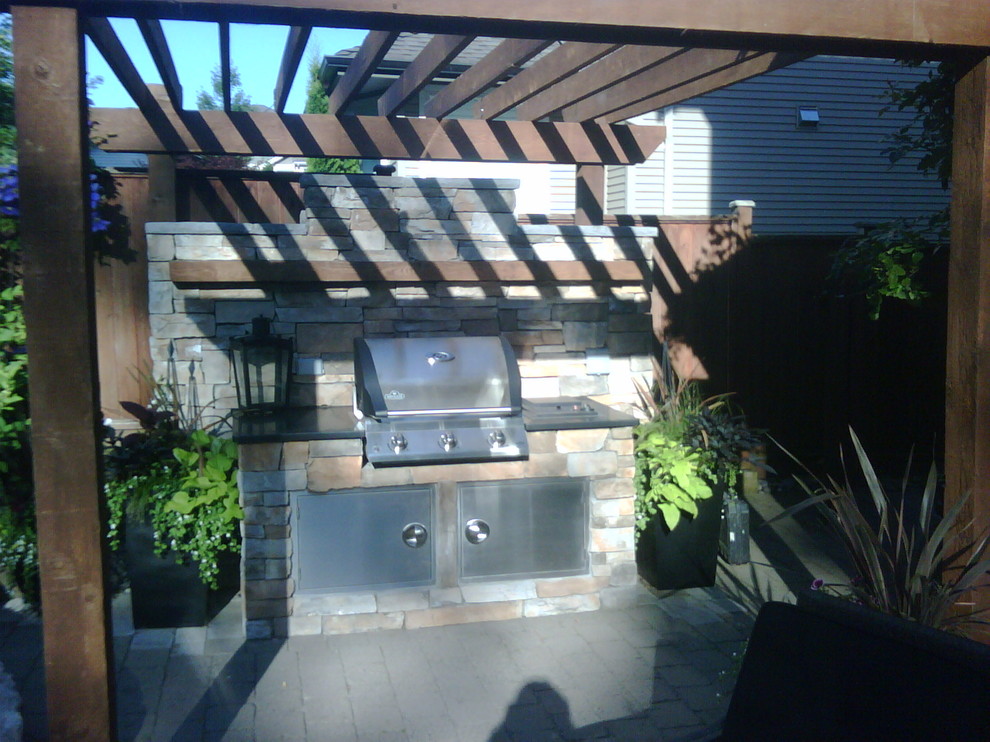 Aménagement d'une grande terrasse arrière craftsman avec une cuisine d'été, des pavés en béton et une pergola.