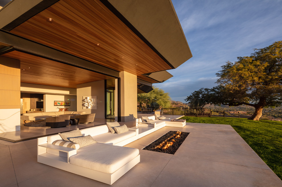 Cette image montre une très grande terrasse arrière design avec un foyer extérieur, une dalle de béton et une extension de toiture.