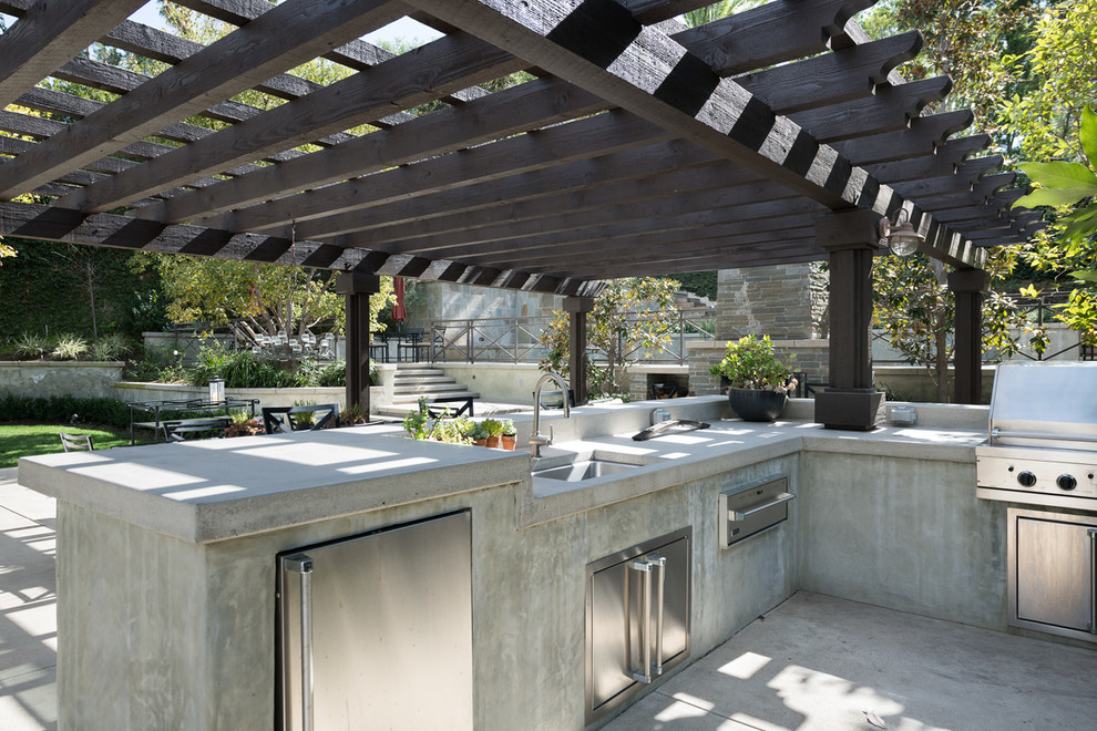 Réalisation d'une grande terrasse arrière minimaliste avec une cuisine d'été, une dalle de béton et une pergola.