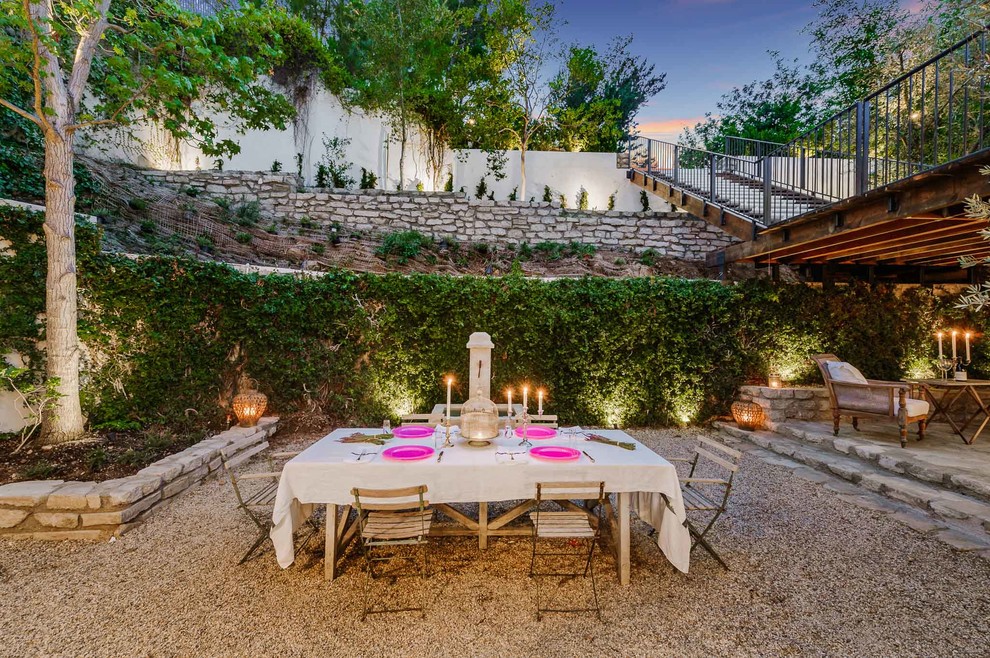 На фото: большой двор на заднем дворе в средиземноморском стиле с фонтаном, покрытием из гравия и навесом с