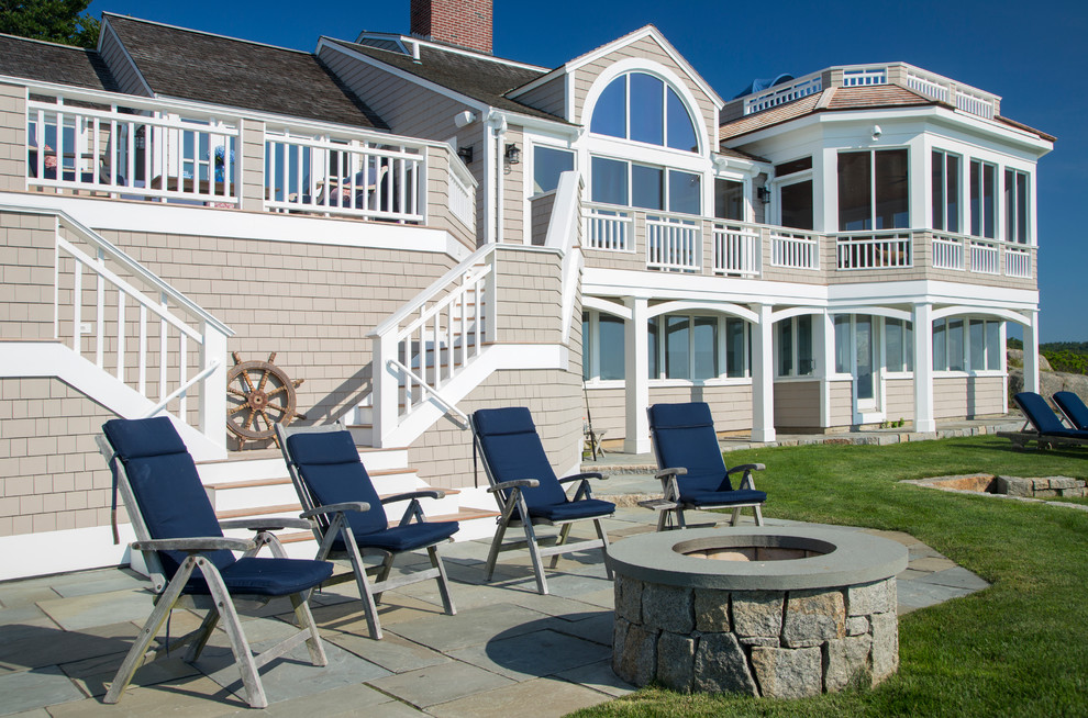 Aménagement d'une terrasse arrière bord de mer de taille moyenne avec un foyer extérieur et des pavés en pierre naturelle.