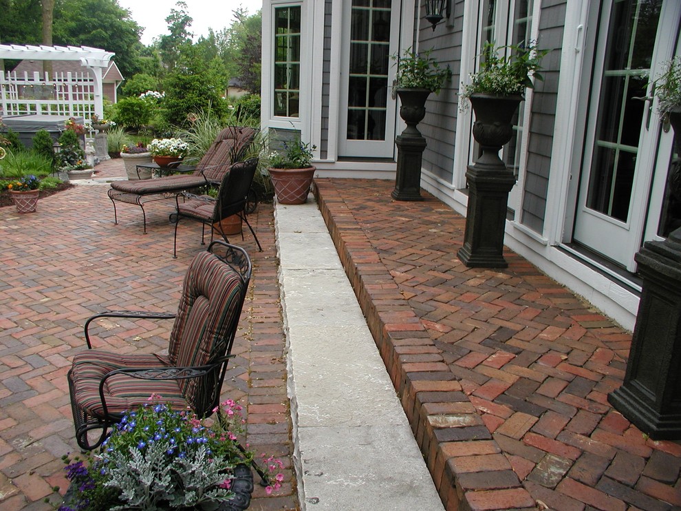 Idée de décoration pour une terrasse avec des plantes en pots arrière tradition de taille moyenne avec des pavés en brique et une pergola.