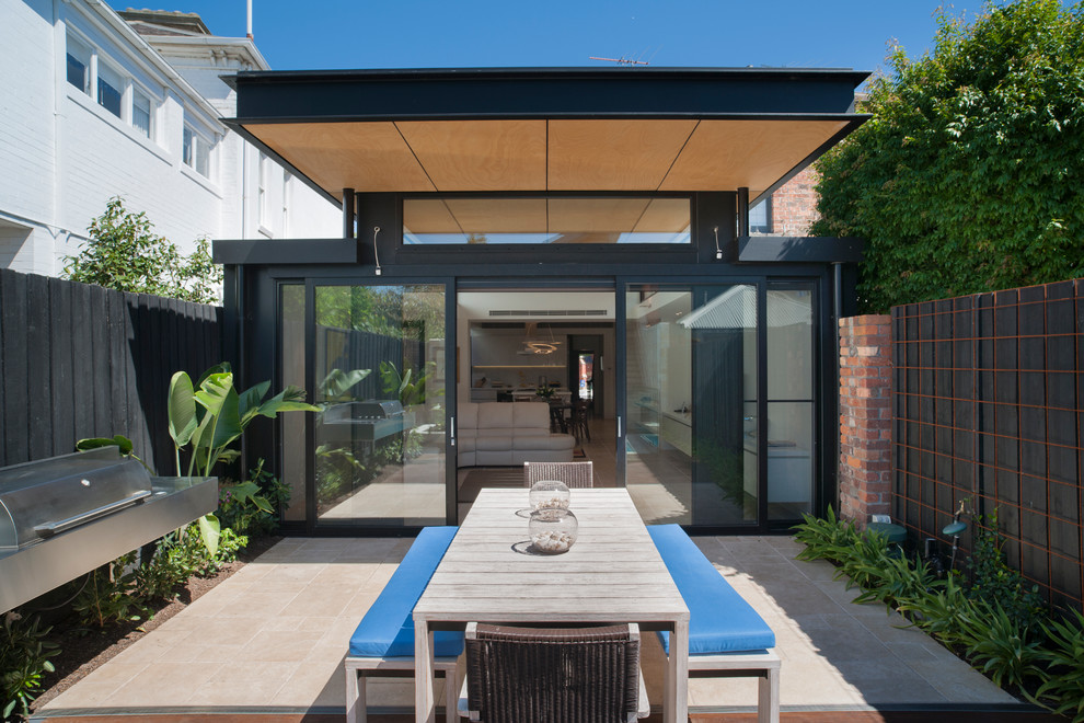 Cette photo montre une petite terrasse arrière tendance avec des pavés en béton et une extension de toiture.