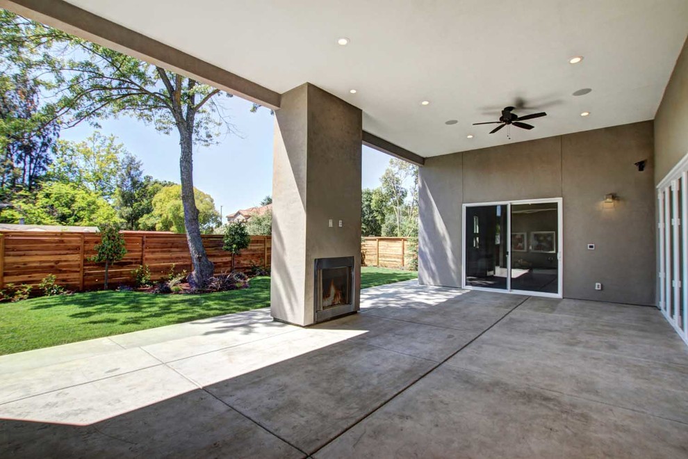 Foto di un ampio patio o portico minimalista dietro casa con un caminetto, un tetto a sbalzo e lastre di cemento