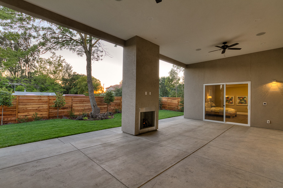 Foto di un ampio patio o portico moderno dietro casa con un caminetto, un tetto a sbalzo e lastre di cemento