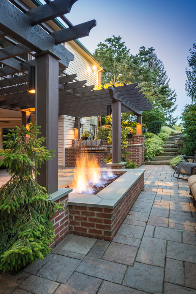 Example of a large urban side yard stone patio kitchen design in Philadelphia with a pergola