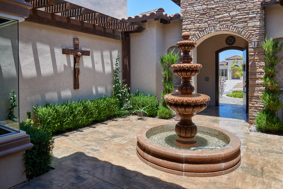 Ejemplo de patio mediterráneo en patio con fuente, suelo de baldosas y pérgola