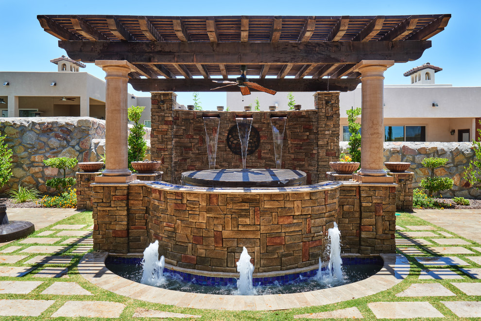 Ejemplo de patio mediterráneo en patio trasero con fuente, adoquines de piedra natural y pérgola
