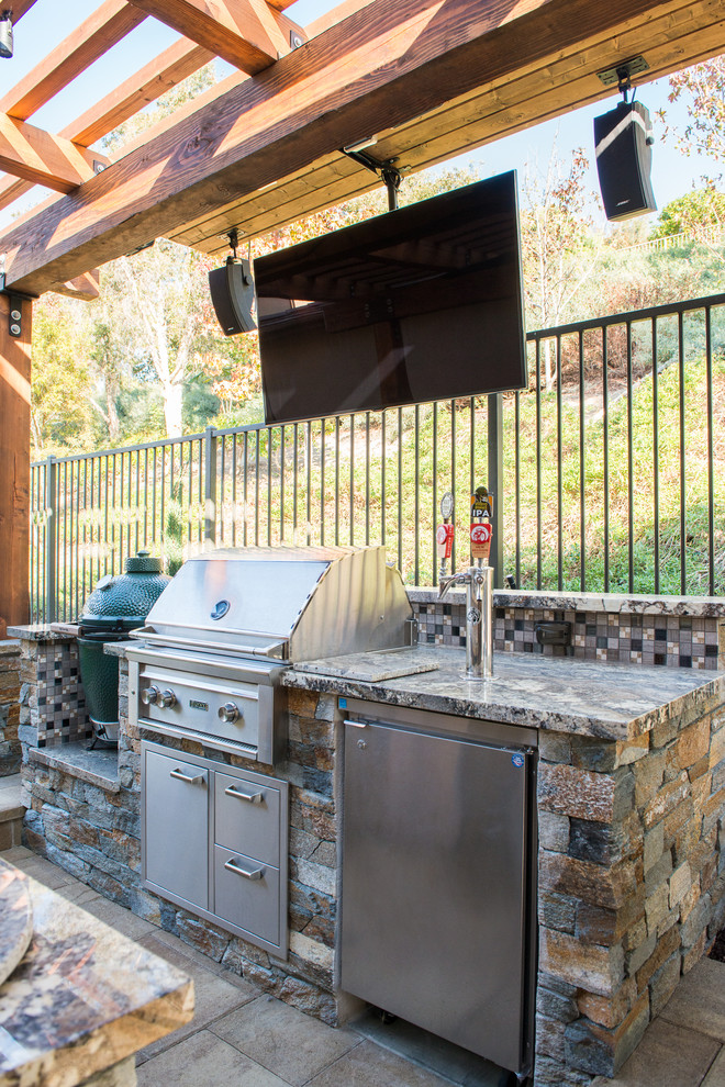 Mid-sized transitional backyard stone patio kitchen photo in Orange County with a pergola