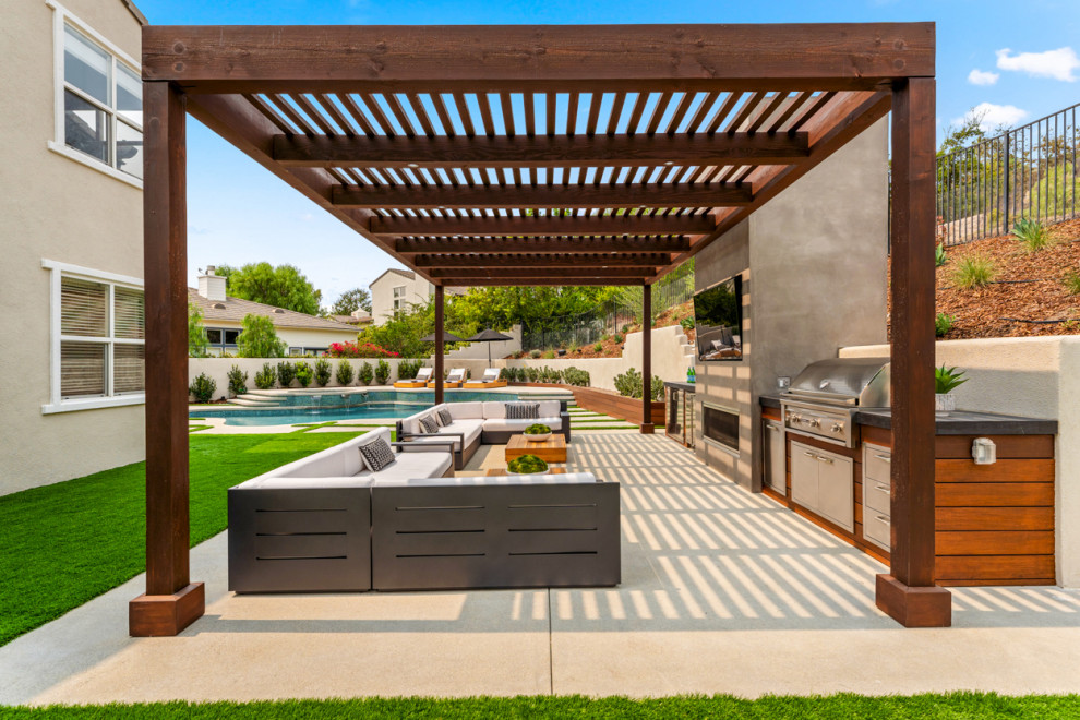 Réalisation d'une grande terrasse arrière design avec une cuisine d'été, des pavés en béton et une pergola.