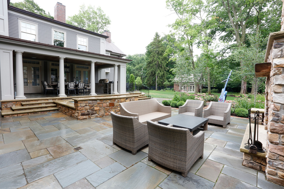Aménagement d'une grande terrasse arrière classique avec un foyer extérieur, des pavés en pierre naturelle et aucune couverture.