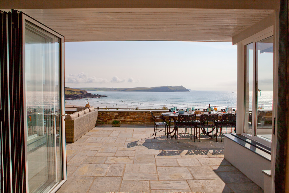 This is an example of a beach style back patio in Cornwall with natural stone paving and no cover.