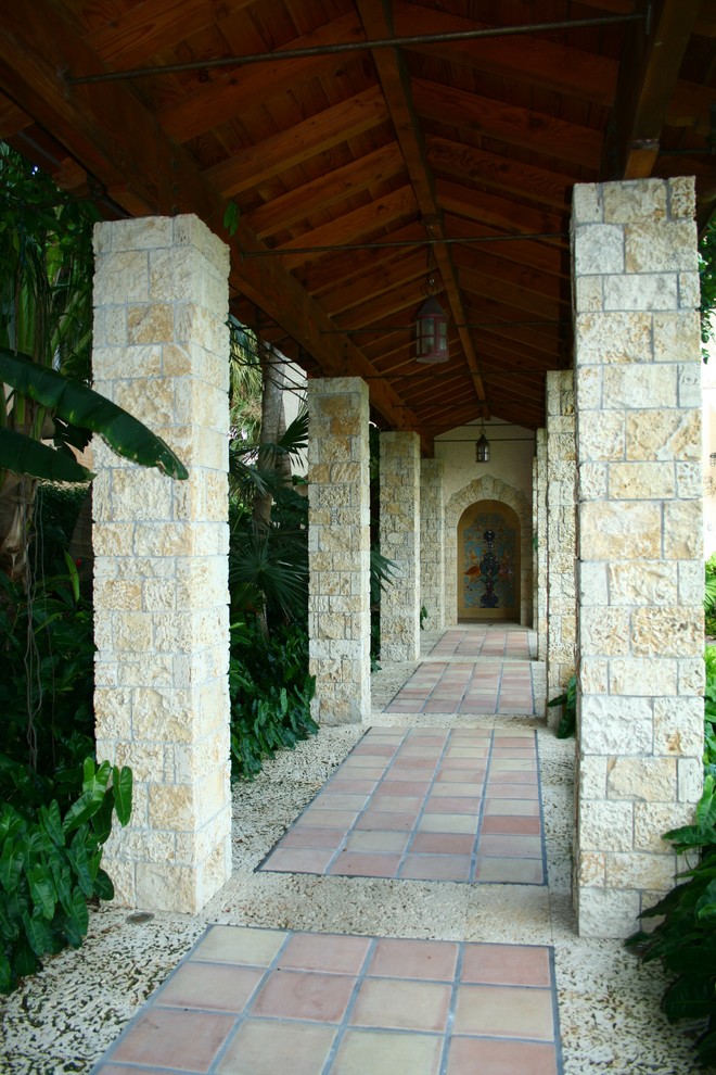 Esempio di un patio o portico mediterraneo con piastrelle e un tetto a sbalzo