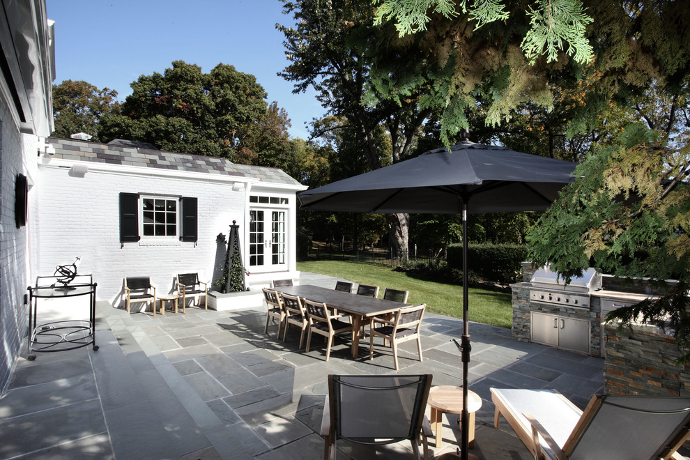 Photo of a large contemporary back patio in New York with an outdoor kitchen, natural stone paving and no cover.
