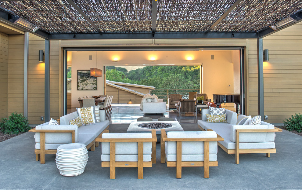 This is an example of a large contemporary side patio in San Francisco with a fire feature, concrete slabs and a roof extension.