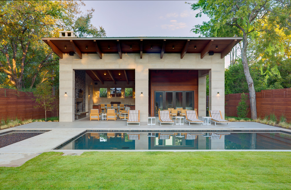 Réalisation d'une grande terrasse arrière design avec un foyer extérieur, une dalle de béton et une extension de toiture.