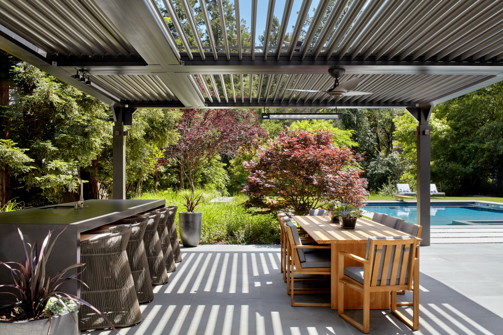 Aménagement d'une très grande terrasse arrière contemporaine avec une cuisine d'été, des pavés en pierre naturelle et une pergola.