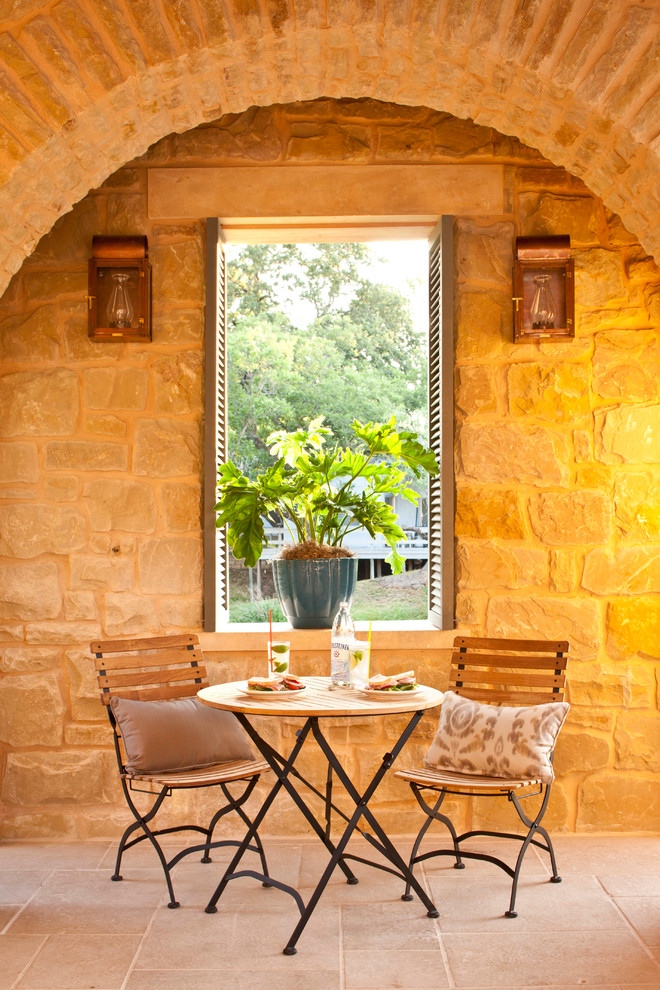 Immagine di un piccolo patio o portico mediterraneo con pavimentazioni in pietra naturale e un tetto a sbalzo