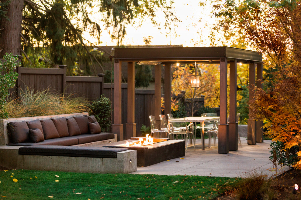 This is an example of a medium sized contemporary back patio in Seattle with a fire feature, concrete slabs and a pergola.