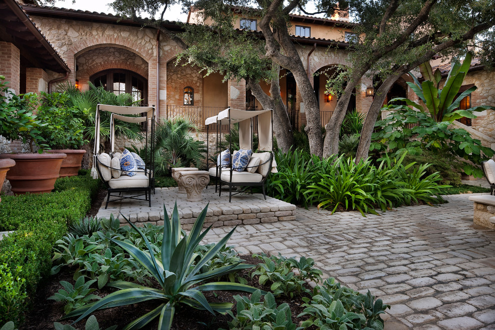На фото: большой двор на заднем дворе в средиземноморском стиле с мощением клинкерной брусчаткой и навесом с