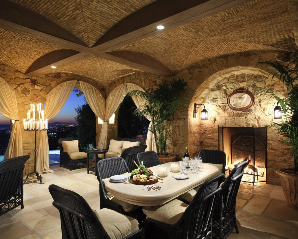 Réalisation d'une grande terrasse arrière méditerranéenne avec un foyer extérieur, des pavés en pierre naturelle et une extension de toiture.