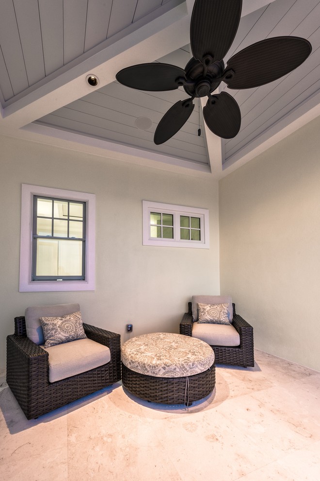 This is an example of a medium sized beach style back patio in Miami with natural stone paving and a roof extension.