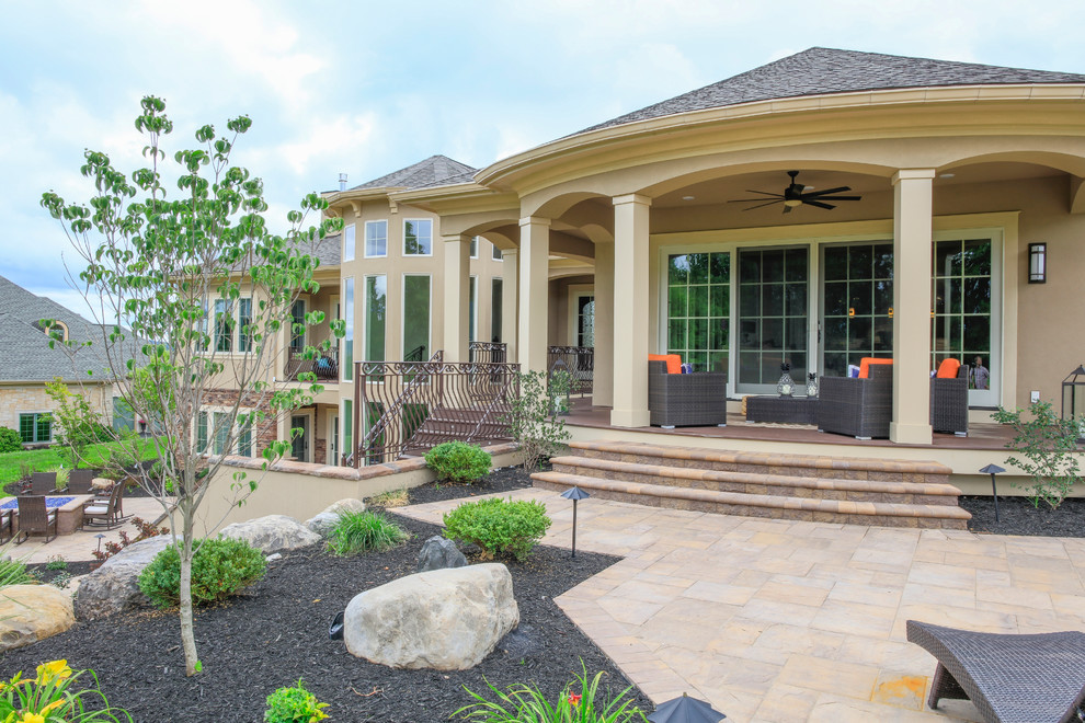 Cette photo montre une très grande terrasse arrière tendance avec un foyer extérieur, des pavés en brique et une extension de toiture.