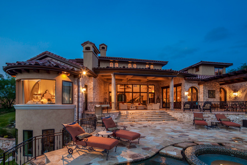 This is an example of an expansive mediterranean back patio in Austin with natural stone paving and a roof extension.