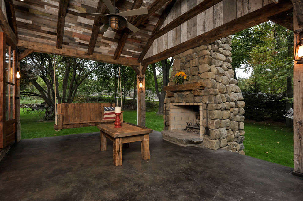 Foto di un grande patio o portico country dietro casa con un focolare, lastre di cemento e un tetto a sbalzo