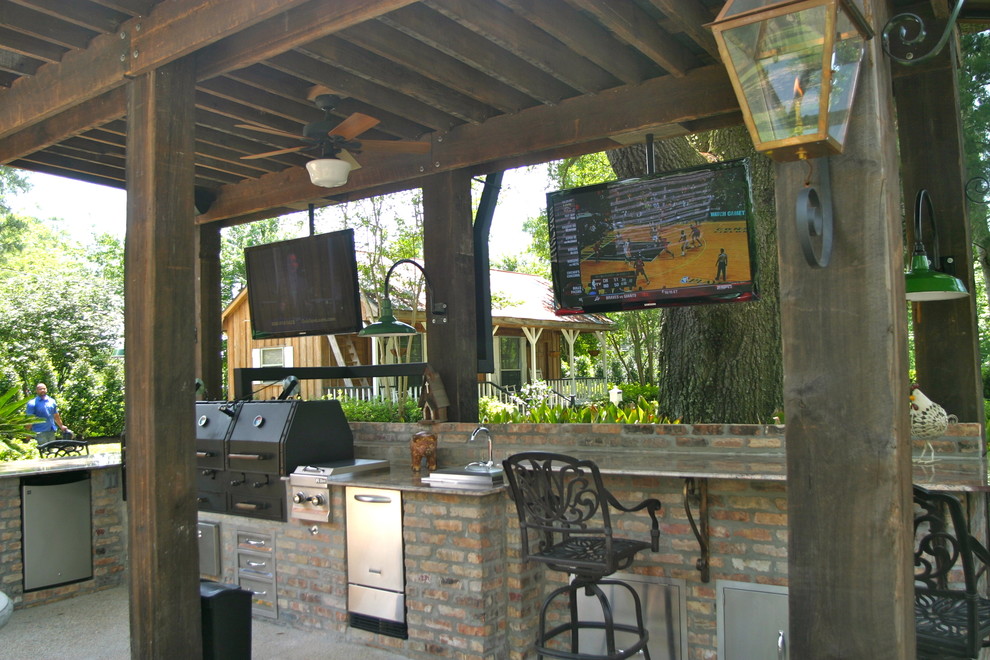 Large traditional back patio in New Orleans with an outdoor kitchen, a pergola and brick paving.