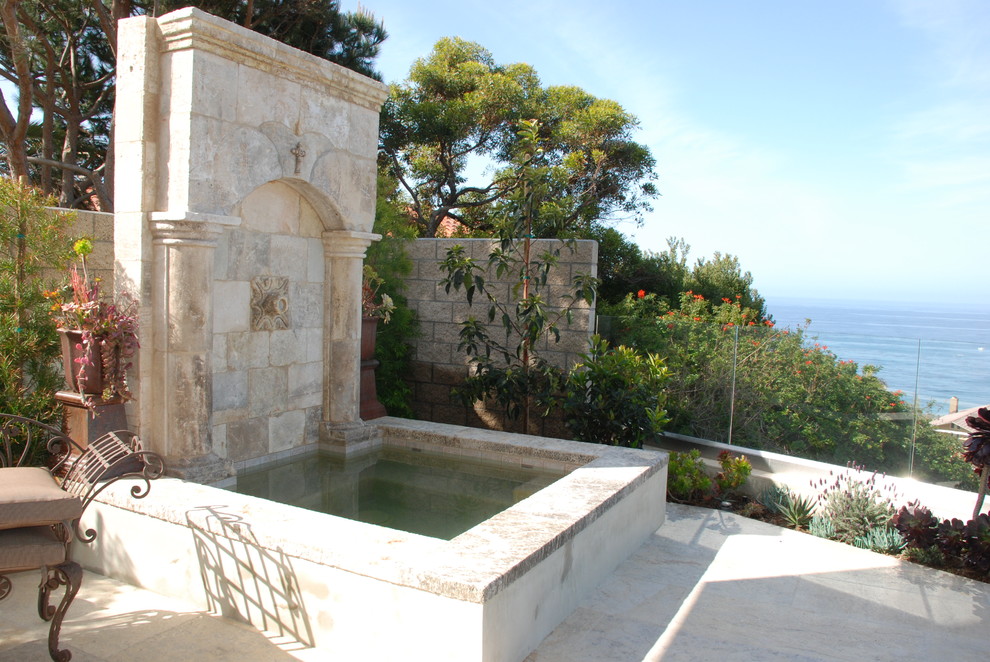 Medelhavsstil inredning av en mellanstor uteplats på baksidan av huset, med en fontän och naturstensplattor