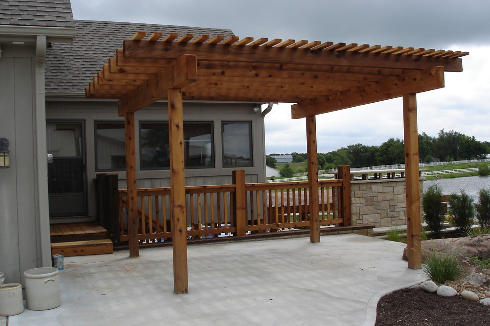 Foto de patio de estilo de casa de campo de tamaño medio en patio trasero con losas de hormigón y pérgola