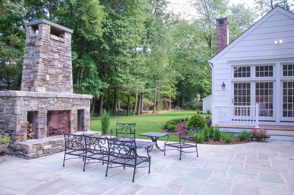 Aménagement d'une grande terrasse arrière classique avec un foyer extérieur, des pavés en pierre naturelle et aucune couverture.
