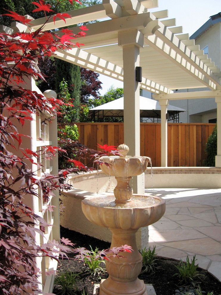 This is an example of a small classic back patio in San Francisco with a water feature, natural stone paving and a pergola.