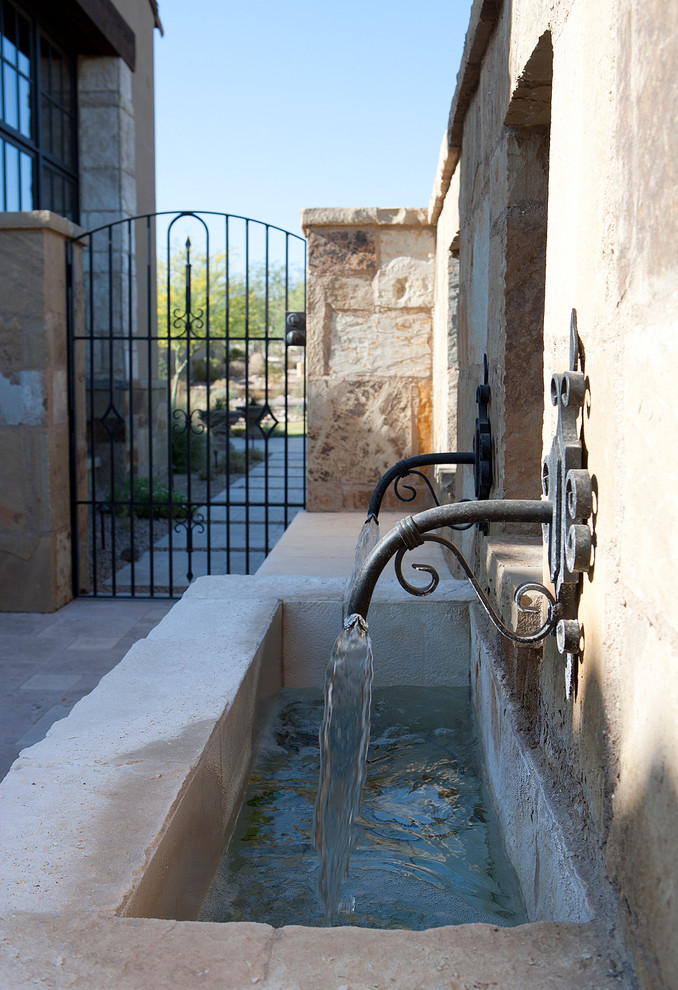 Ejemplo de patio mediterráneo extra grande en patio lateral con fuente y adoquines de piedra natural