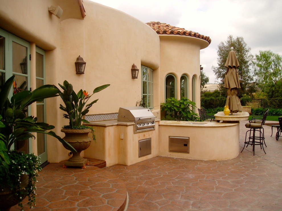 This is an example of a mediterranean back patio in San Diego with an outdoor kitchen and natural stone paving.
