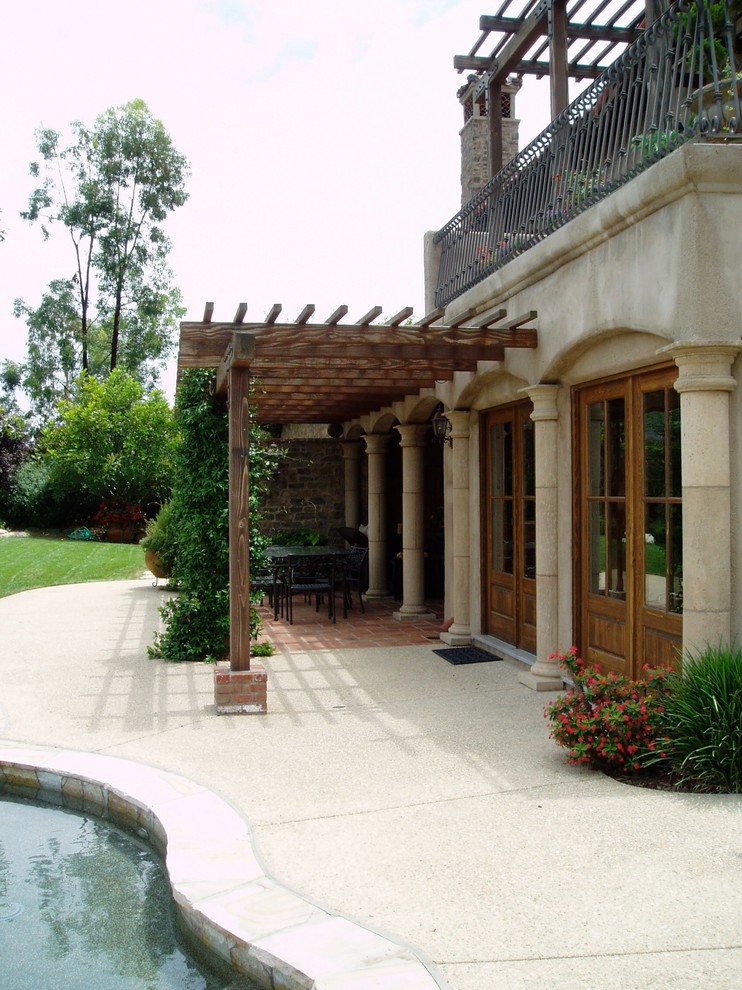 Immagine di un patio o portico mediterraneo dietro casa con un caminetto, pavimentazioni in cemento e una pergola