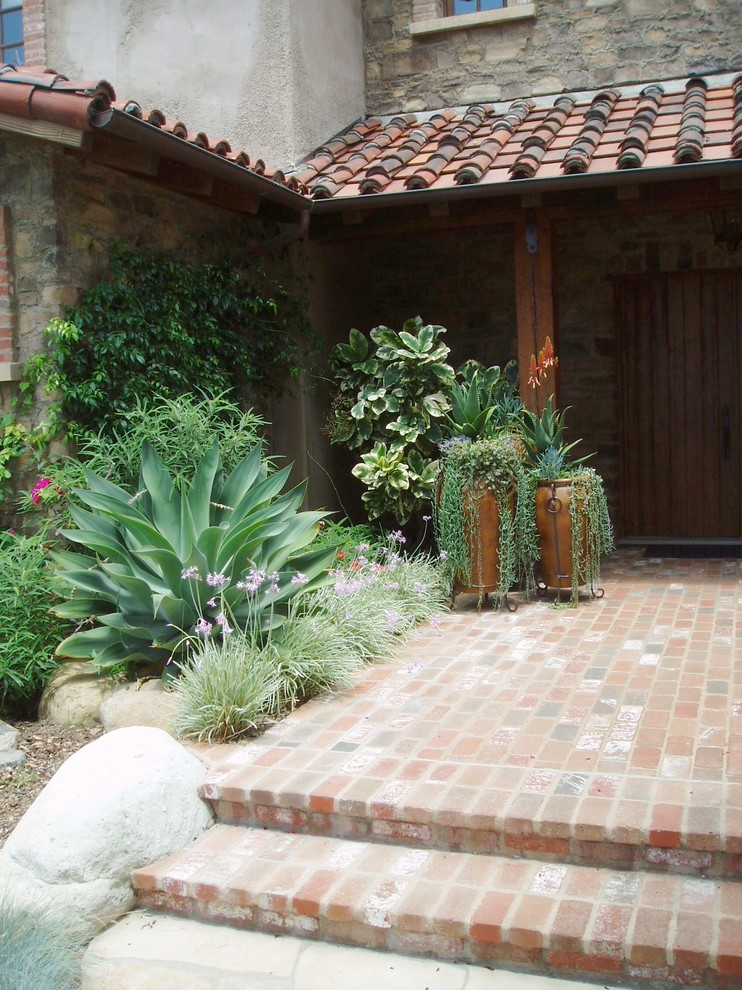 Esempio di un patio o portico mediterraneo con pavimentazioni in mattoni