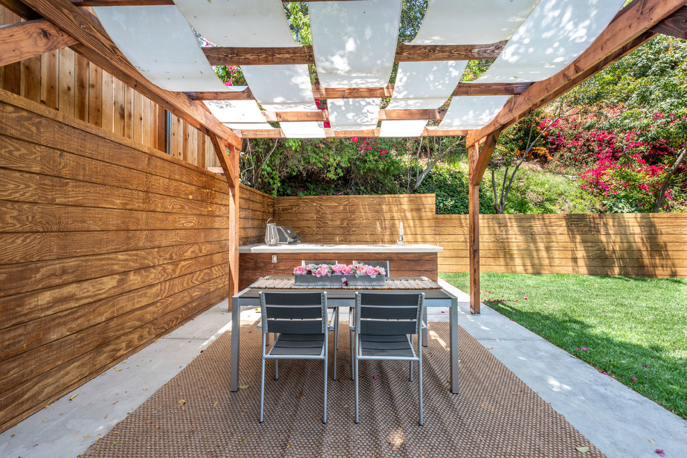 На фото: пергола во дворе частного дома среднего размера на заднем дворе в современном стиле с летней кухней и покрытием из бетонных плит