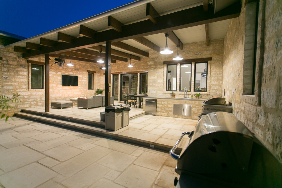 Photo of a farmhouse patio in Austin with a fire feature, natural stone paving and an awning.
