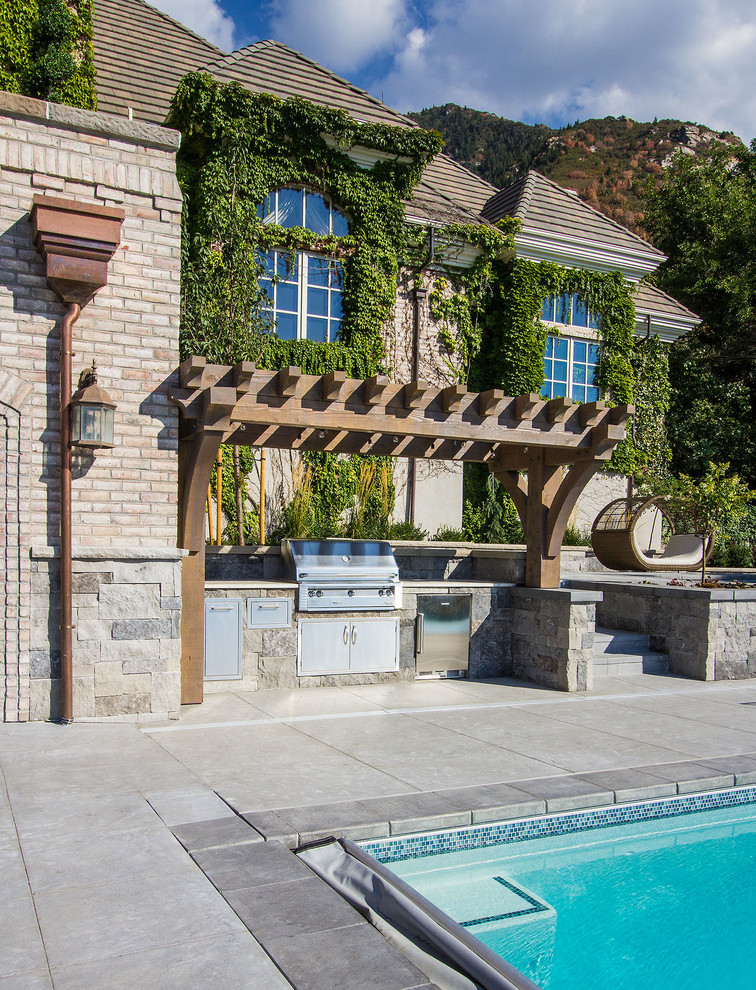 Cette photo montre une grande terrasse arrière chic avec une cuisine d'été, une dalle de béton et une pergola.