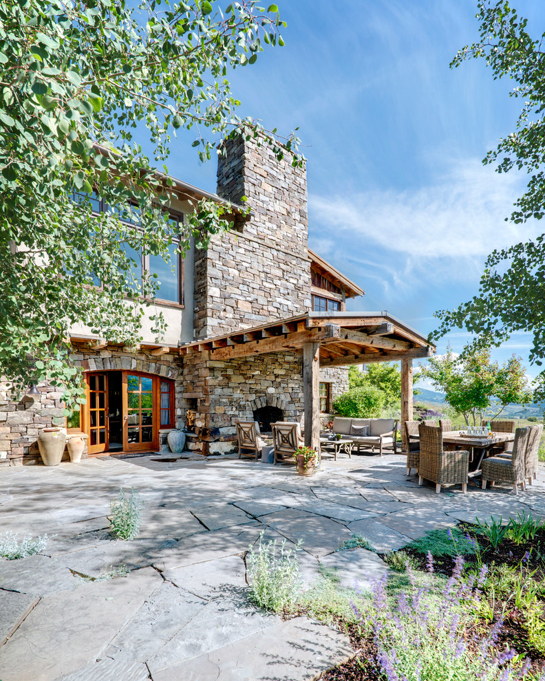 Cette image montre une grande terrasse arrière chalet avec un foyer extérieur, des pavés en pierre naturelle et un gazebo ou pavillon.