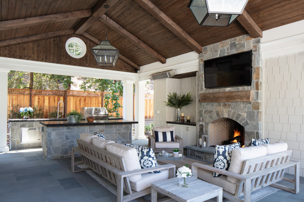 Exemple d'une grande terrasse arrière bord de mer avec une cuisine d'été, des pavés en pierre naturelle et une extension de toiture.